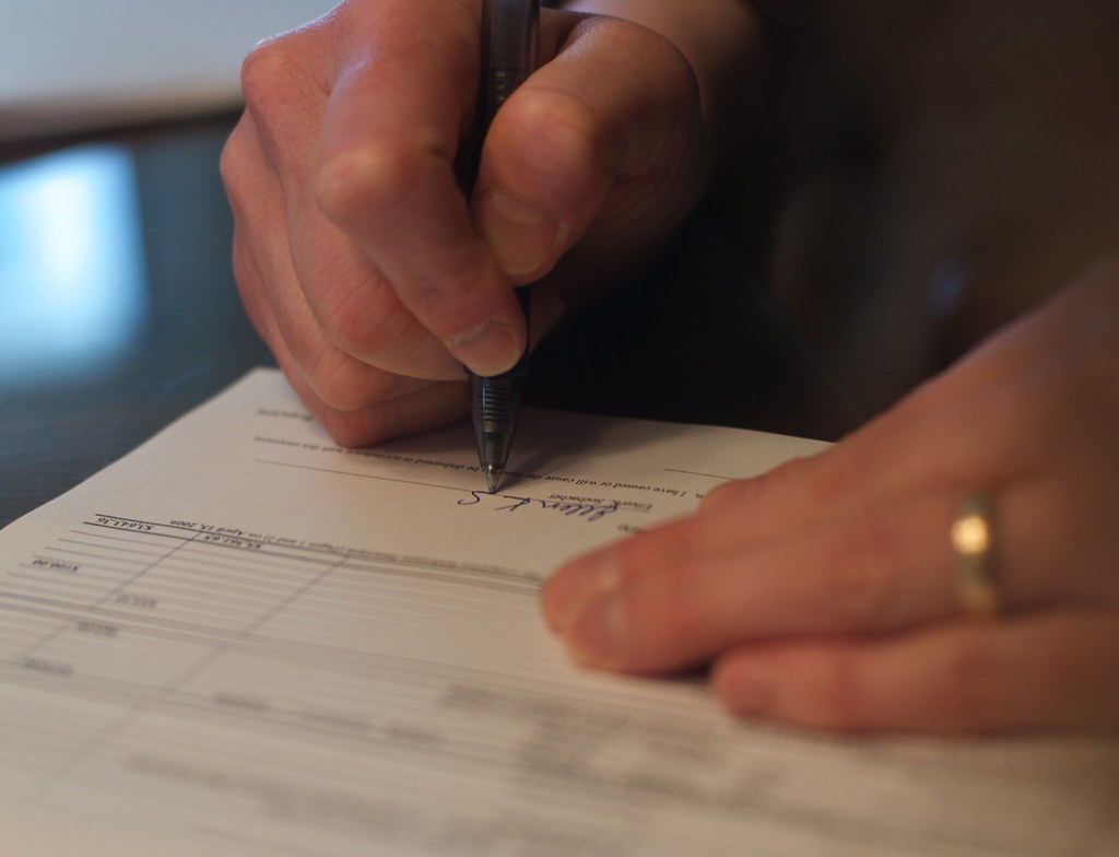 Hand holding a pen signing a printed form on a desk