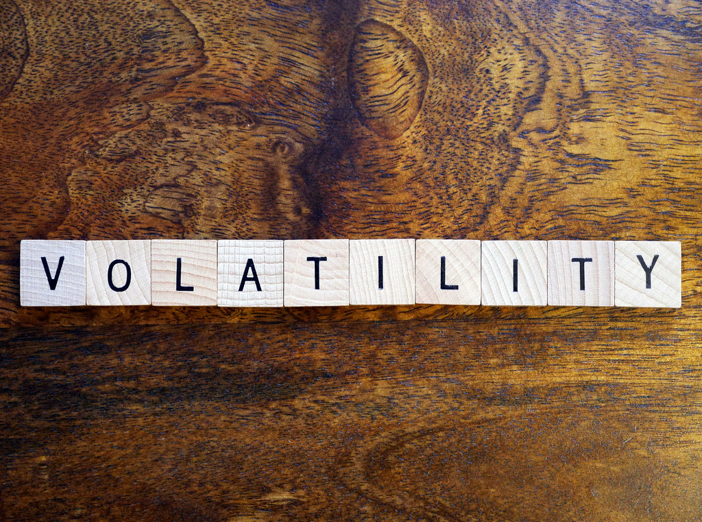 Letter tiles spelling VOLATILITY on a dark wood grain surface